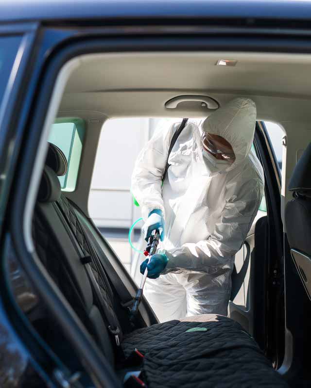 persona con vestimenta de protección desinfectando un automóvil